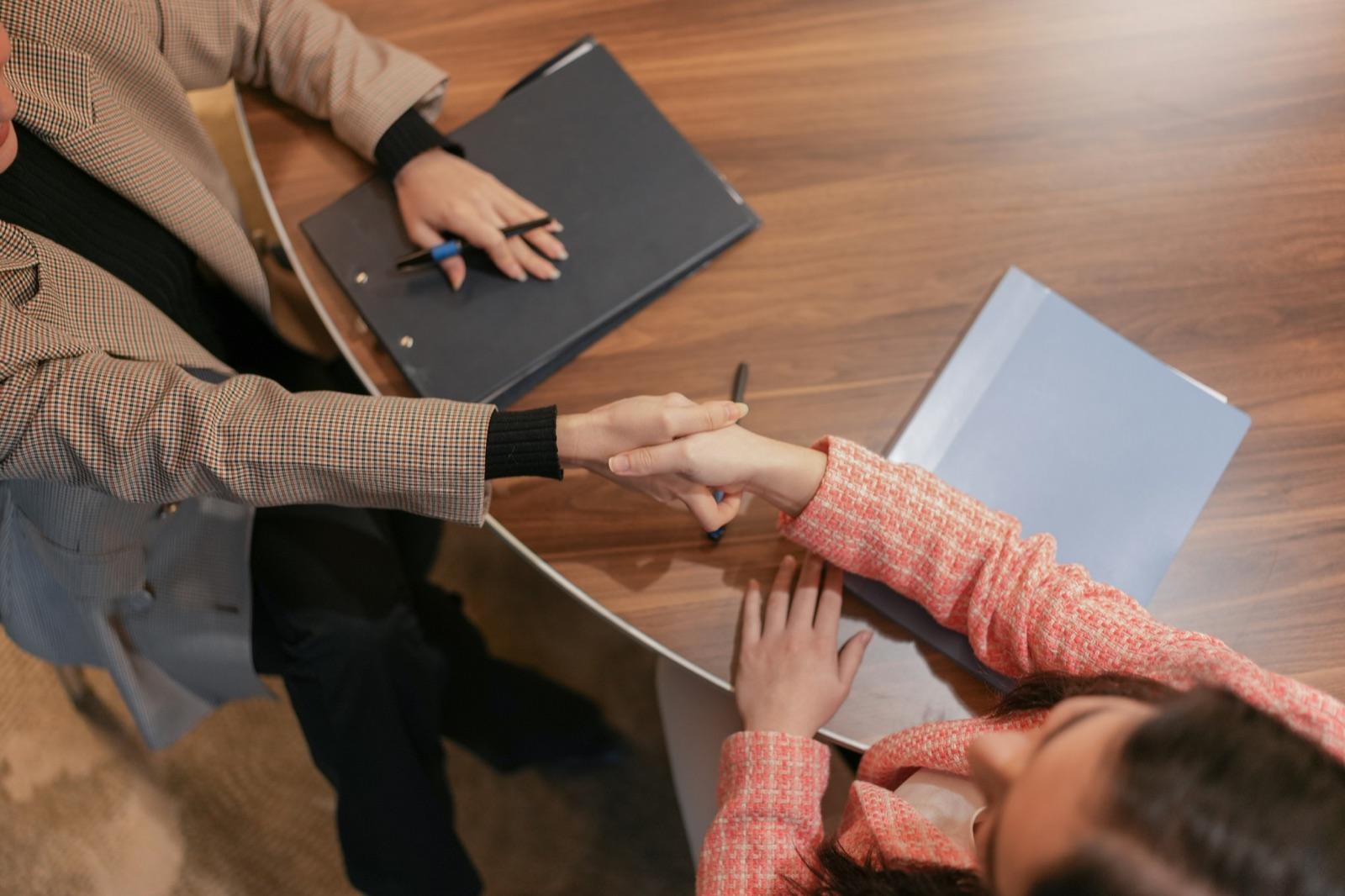 Two people shaking hands across a table during a client meeting